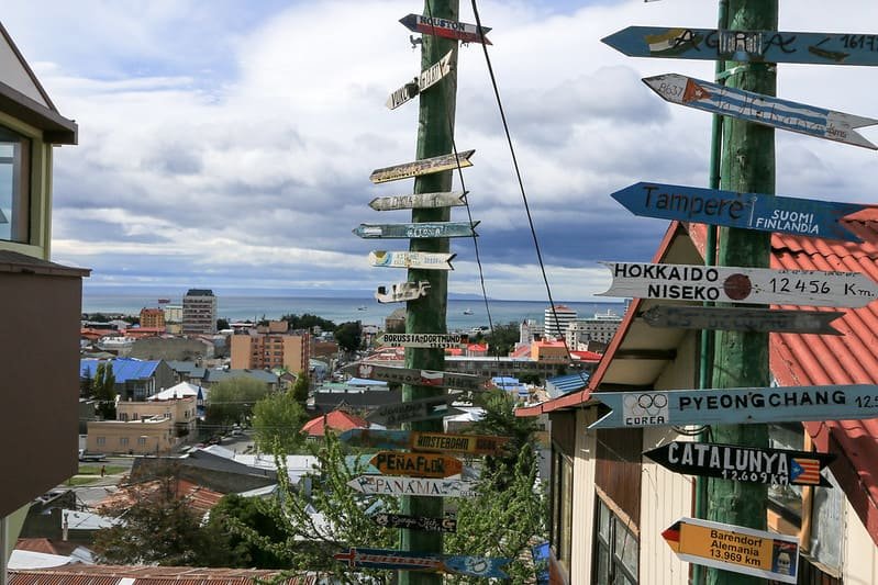 Signpost with distances to world cities above the rooftops of Punta Arenas