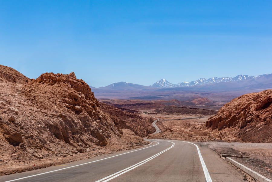 Desert road from Calama to San Pedro de Atacama with volcanoes ahead
