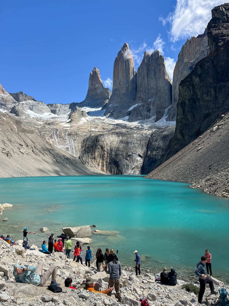 Hikers resting by the turquoise lagoon at the Base Las Torres viewpoint