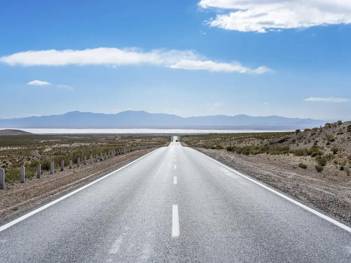 Paved road descending toward the white salt flats of Salinas Grandes on the way from San Pedro de Atacama to Salta
