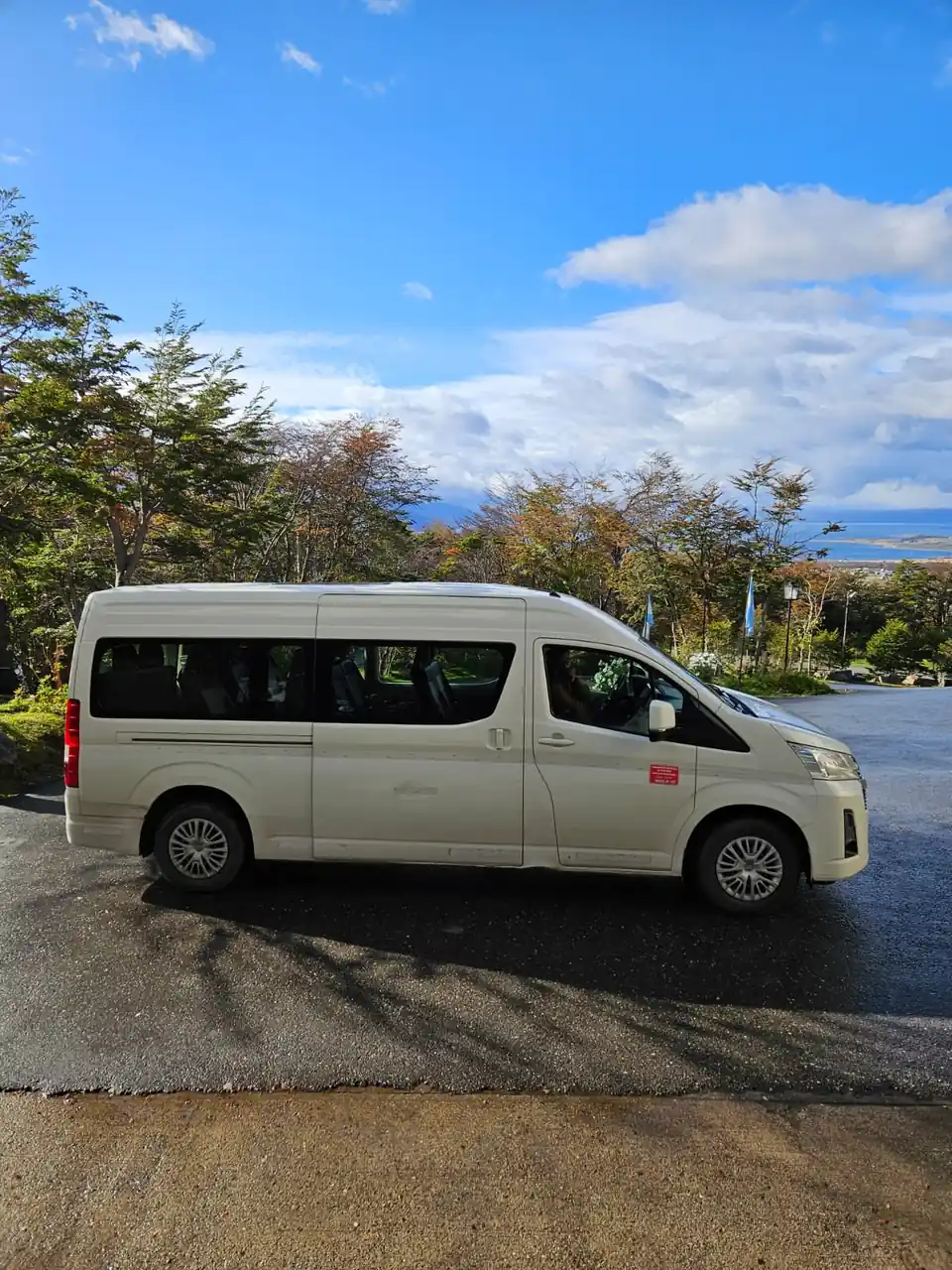 White private transfer minibus parked above Ushuaia with the Beagle Channel in the background